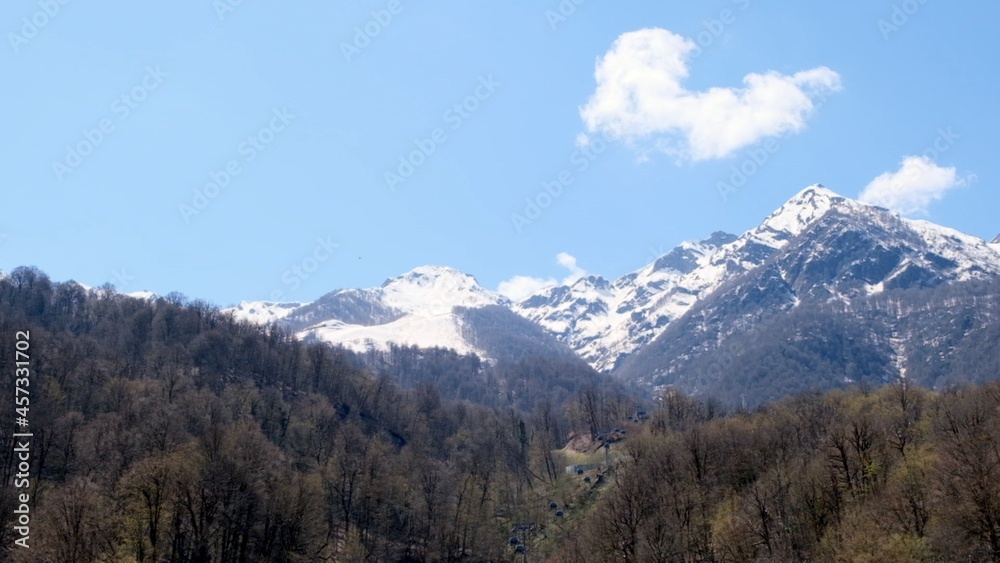 beautiful landscape of snow-capped mountains with white clouds on blue sky on a sunny day at Krasnaya Polyana in Sochi, Russia. Famous ski resort