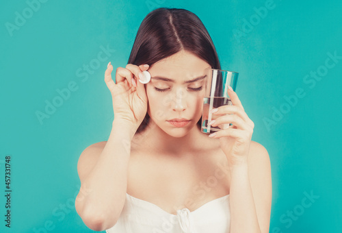 Woman taking drugs to releave headache. Brunette take some pills, holds glass of water, isolated on blue photo