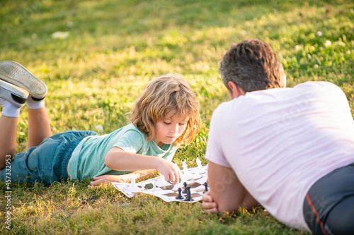 happy family of dad and son kid playing chess on green grass in park outdoor, tutorship