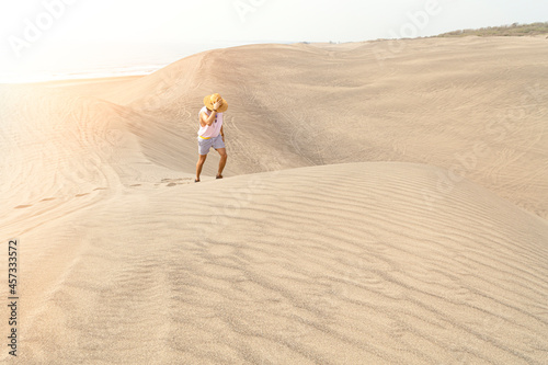 Young male holding his hat  walking on sand dunes during golden hour