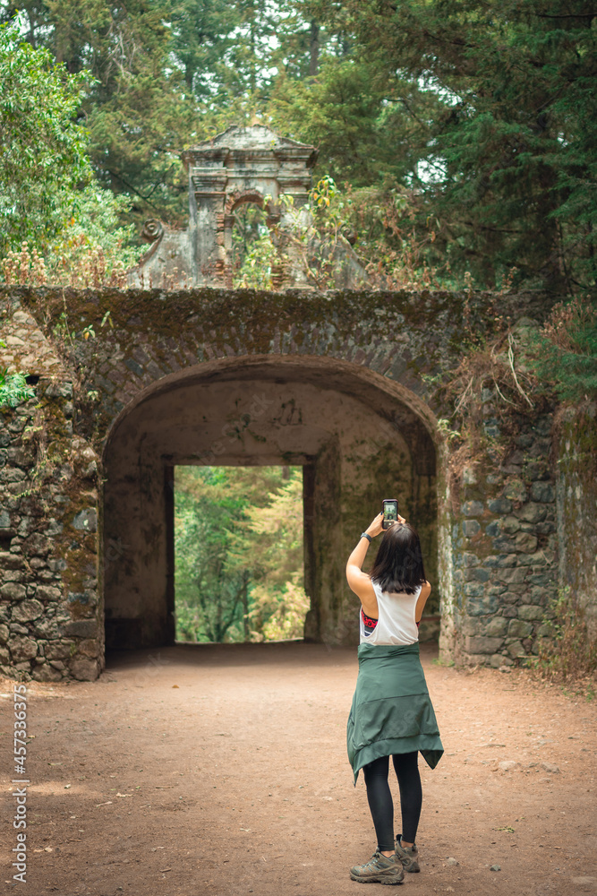Young woman from behind taking a photo to the arches of the old road.