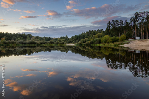 Summer landscape in the evening by the river. Dramatic clouds are reflected in the water. Intense colors in the landscape after sunset.