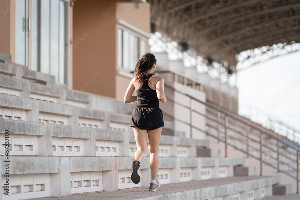 A healthy adult Asian woman running up on concrete stairs of the city stadium to strengthen body A healthy adult Asian woman running up on concrete stairs of the city stadium to strengthen body