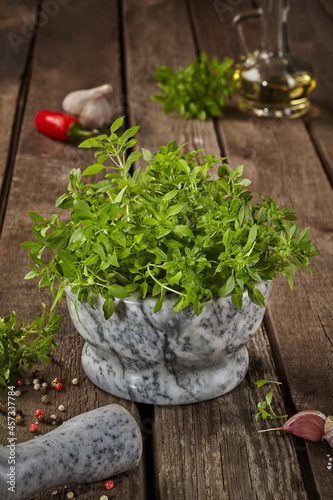 Fresh small-leaved basil in mortar with condiments on wooden table