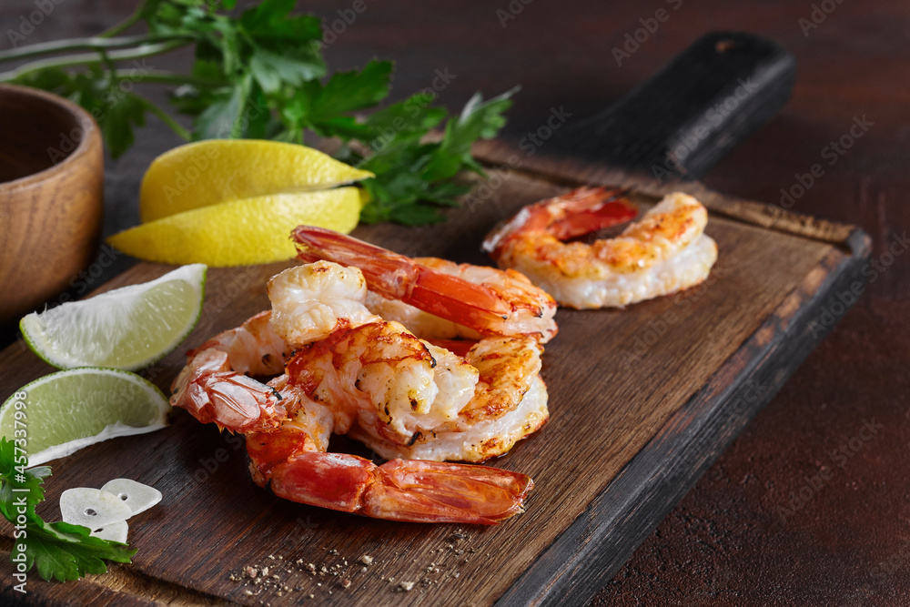 Grilled prawn tails with lemon, lime, parsley, garlic on wooden board