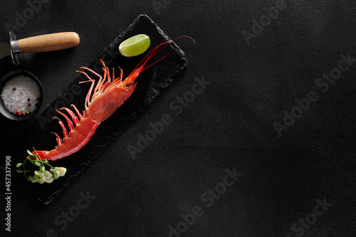 Boiled king prawn with condiments and shrimp knife on black background