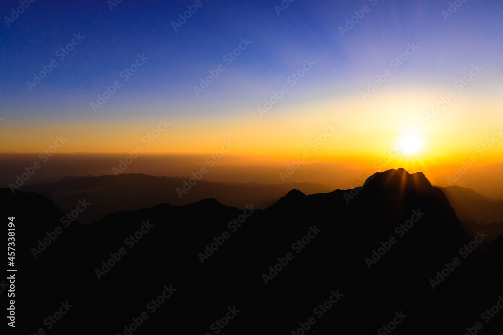 A stunning sunset or sunrise scene of silhouette mountain peaks and purple ridges with the twilight background, the blue sky and the pink-yellow skyline, captured at chiangmai, thailand
