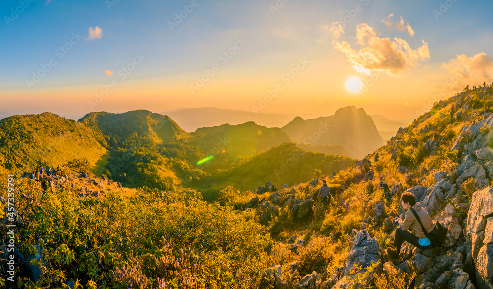 A tourist with beautiful mountain peaks topped with vivid sky, cloud and blast horizon sun, and decorated with camera flares