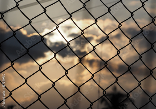 Steel mesh fence with blurred sunset background.