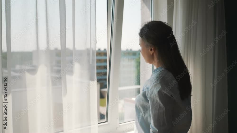 Woman opening curtains in her apartment. Woman opening curtains in her apartment.