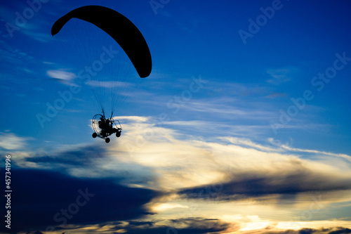 A Silhouette paramotor pilot flying over a lake with the sunset sky background