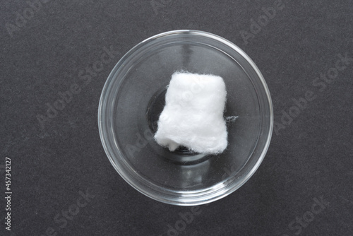 cotton ball in a clear glass bowl on a dark gray paper background