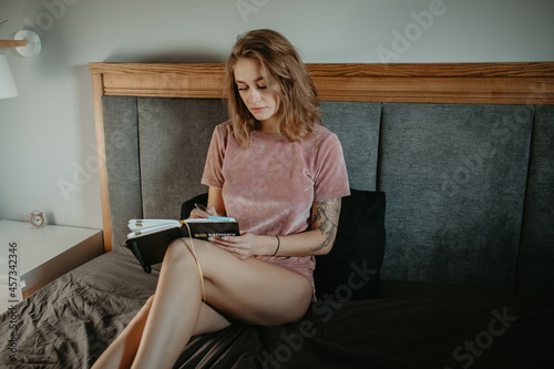 beautiful girl sitting in bed and writing in a notebook 