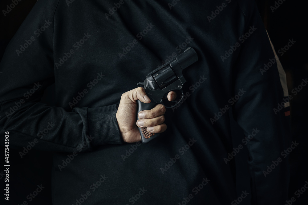 Man in dark clothes with revolver on his back. Criminal with hand gun. Person holds firearm for attack or defense. Man in dark clothes with revolver on his back. Criminal with hand gun. Person holds firearm for attack or defense.