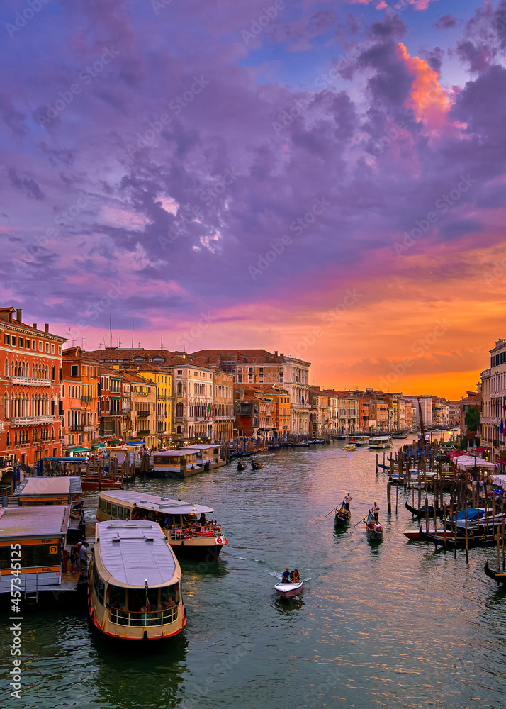 Sunset view of Grand Canal, Venice, Italy. Vaporetto or waterbus station, boats, gondolas, beautiful sunset clouds, UNESCO heritage. Vertical shot