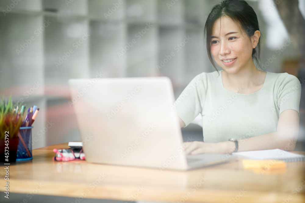 Portrait of Asian young female Businesswoman working on laptop computer doing finances,accounting analysis,report,data and pointing graph at the office.