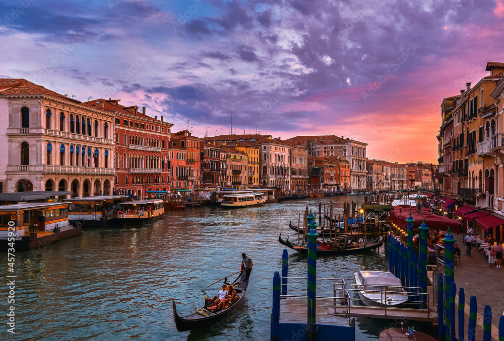 Fototapeta premium Sunset view of Grand Canal, Venice, Italy. Vaporetto or waterbus station, boats, gondolas moored by walkways, beautiful sunset clouds, UNESCO heritage