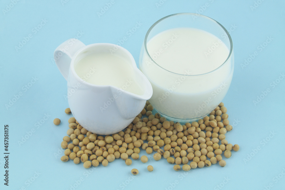 Soy milk in jug and glass and soy beans on blue background Soy milk in jug and glass and soy beans on blue background