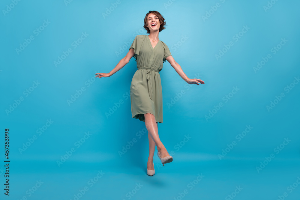Full size photo of cute young brunette lady dance wear khaki dress stilettos isolated on blue background Full size photo of cute young brunette lady dance wear khaki dress stilettos isolated on blue background