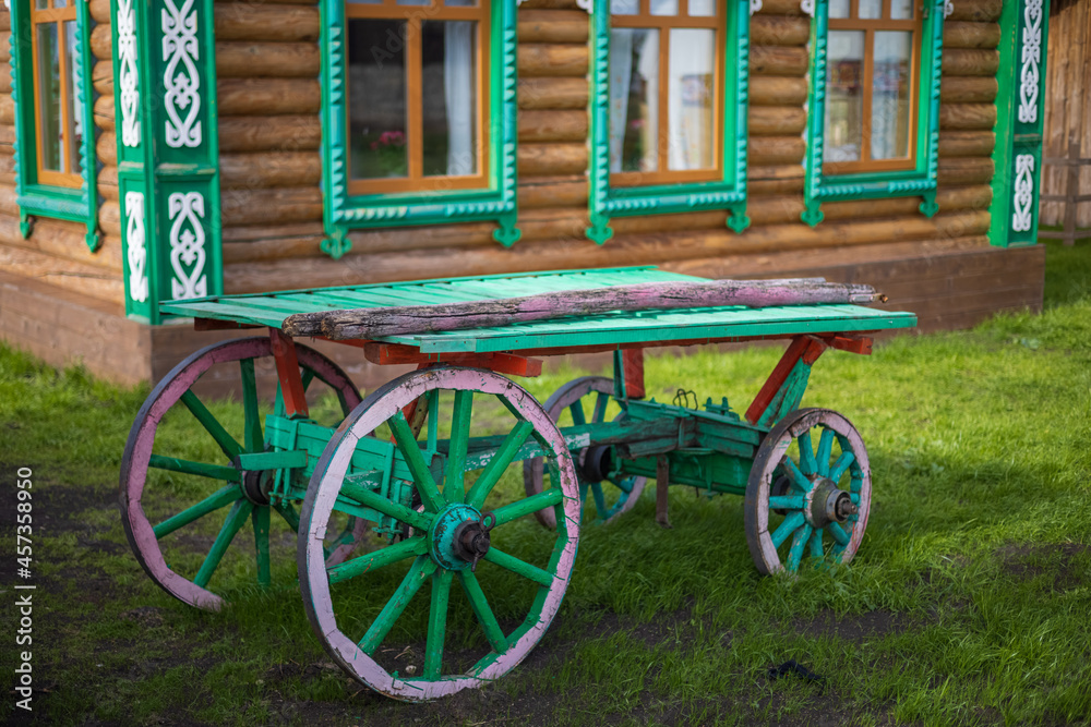 An old village cart against the backdrop of a traditional village log house.
