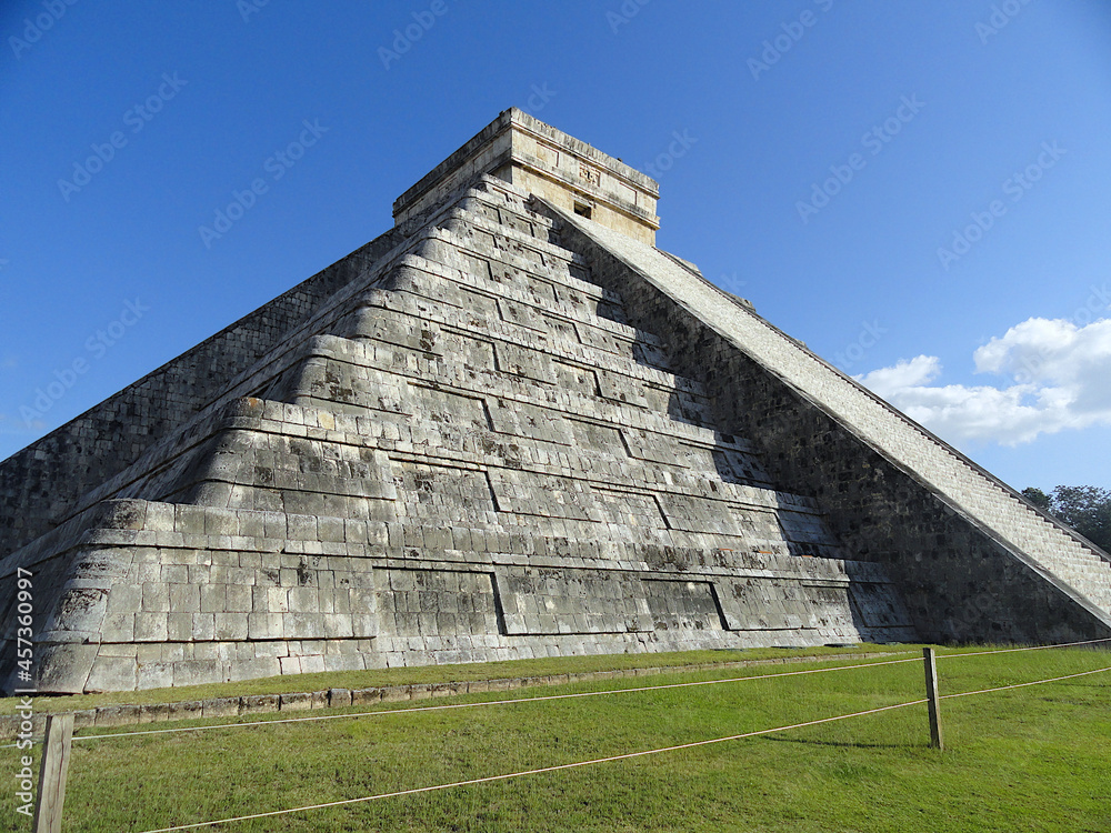 The ancient maya pyramid at the archaeological zone at Chichen Itza. View from the bottom. Temple of Kukulcan, Mexico. Blue sky and green grass.
 