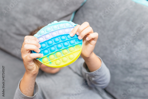 Schoolboy 10s boy lying on the couch and playing with sensory pop it fidget toy at home. Kid playes stress and anxiety relief fidgeting game after learning. photo