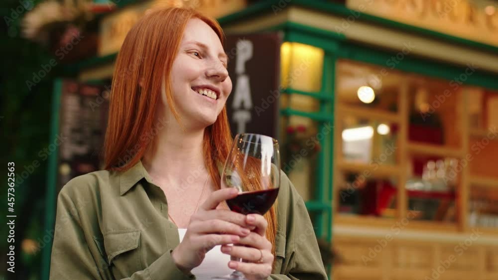 A close up shot of a ginger haired young woman, wearing a green blouse with a white top, she s drinking some wine while she is conversing and laughing outside in a park A close up shot of a ginger haired young woman, wearing a green blouse with a white top, she s drinking some wine while she is conversing and laughing outside in a park