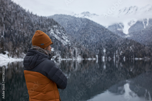 Fotografi Man in warm puffy jacket of orange and black colors wearing hat and scarf, admir