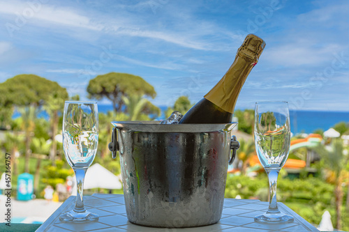 A bottle of sparkling wine in an ice bucket and two glasses on the balcony against the background of the sea and the resort