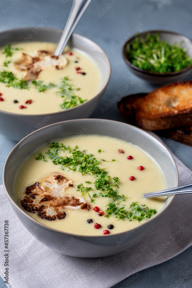 Cauliflower soup on gray tabletop, creamy flower soup with toasted bread, garden cress, red and black peppercorns. vegetarian healthy food concept