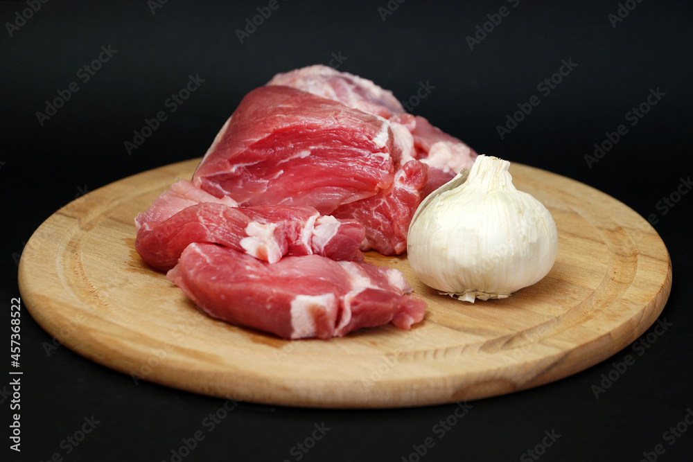 pork meat and garlic on a round wooden board on a black background
