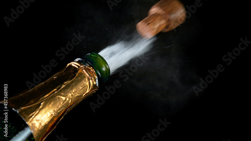Freeze motion of Champagne explosion with flying cork closure, opening champagne bottle closeup isolated on black background. © Lukas Gojda