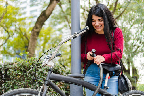 Young latin woman locking her bicycle in a post in the park