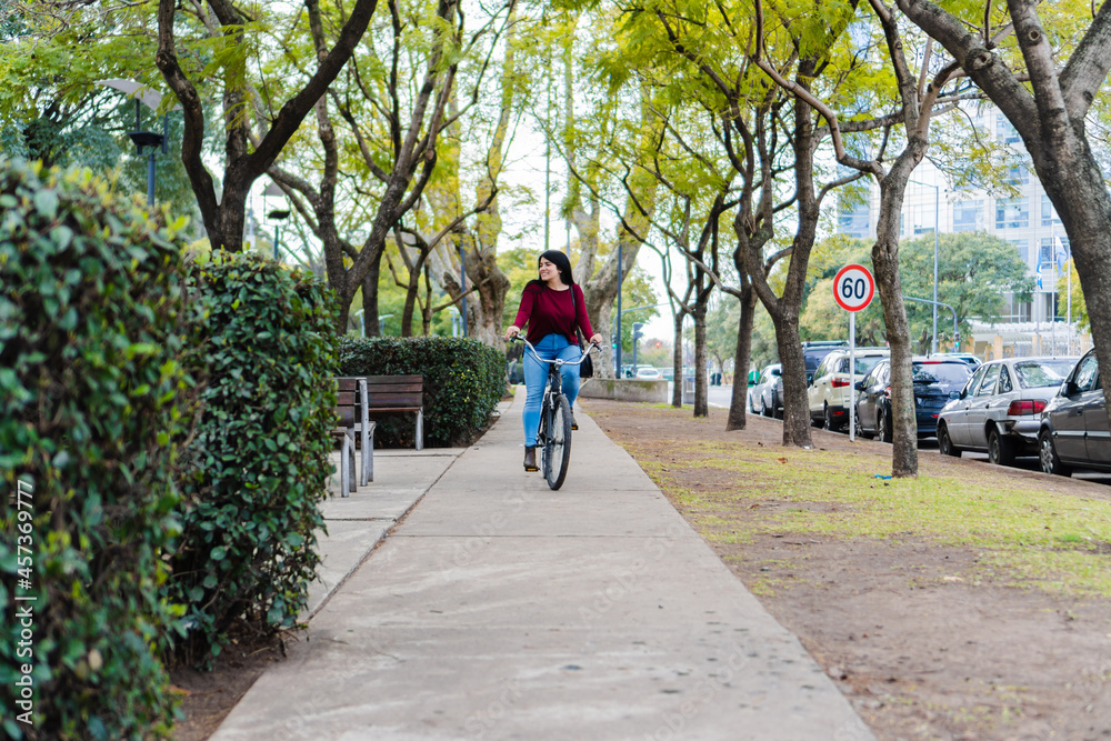 Young latin woman riding her bike on the sidewalk in a sunny day
