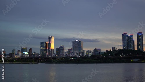 Night Seoul from the Riverbank of Han River on Colorful Sunset, Landscape Of Skyscrapers like Glass Tower, Trade Tower, and Asem Tower Under Sunlight, Yacht Pass by when People Paddleboarding on River photo