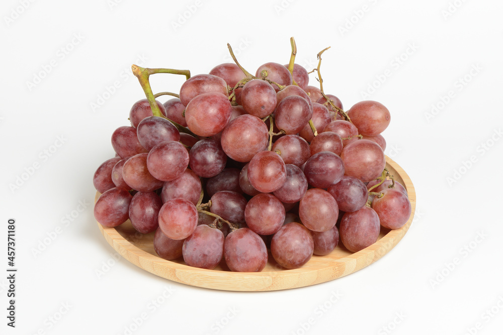 Uva rojas en un plato de madera sobre fondo blanco