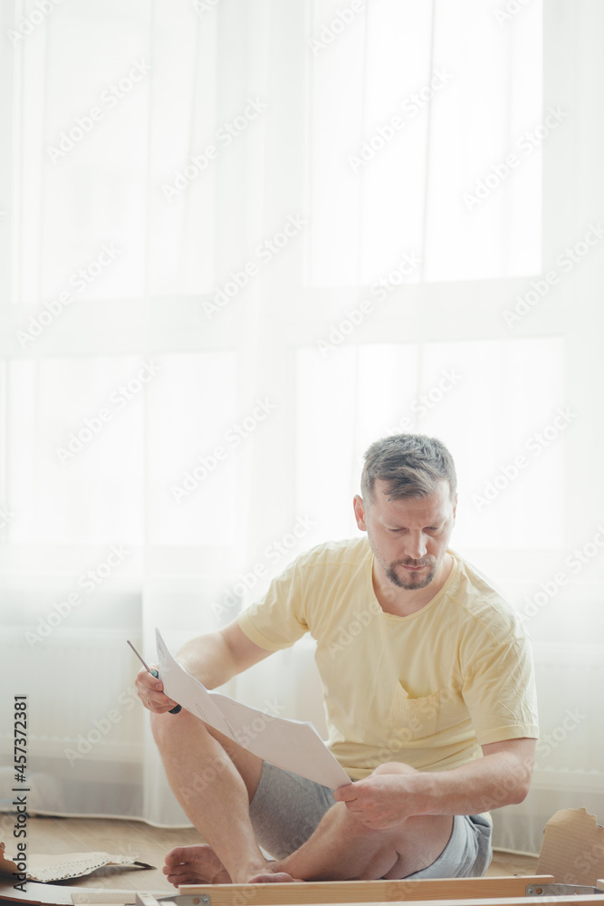 Young attractive man in a yellow T-shirt assembles furniture Young attractive man in a yellow T-shirt assembles furniture