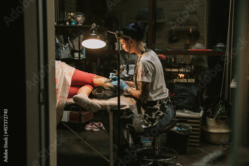 Portrait of a woman tattoo master showing a process of creation tattoo on a hand under the lamp light. photo