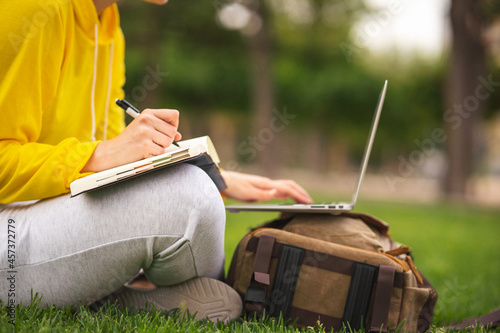 Spanish student working sitting on the grass with laptop and agenda
