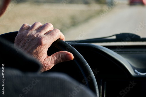 Hands of an elderly man holding the steering wheel of a vehicle photo