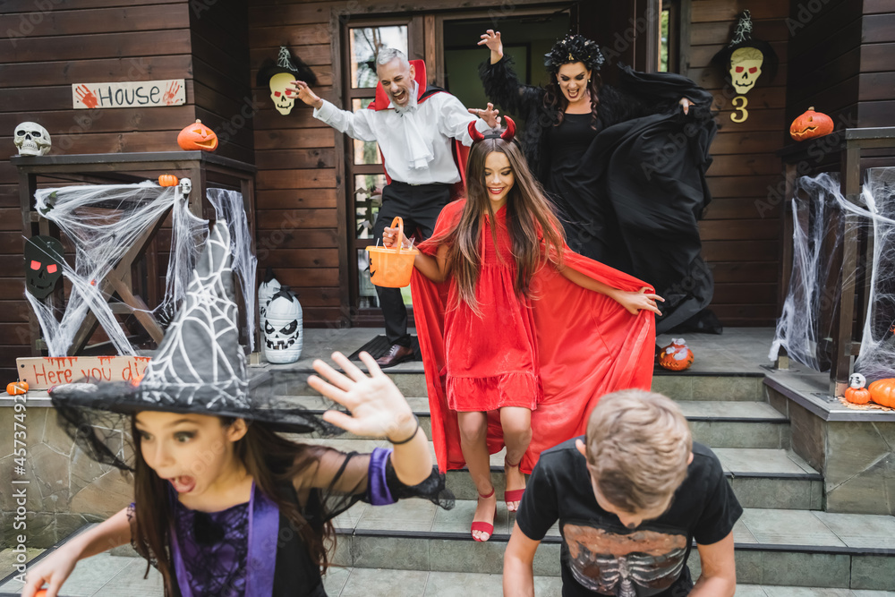 thrilled family with halloween attributes shouting while running out cottage