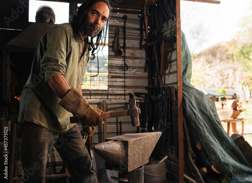 Long-haired blacksmith showing mace on an anvil in his workshop.