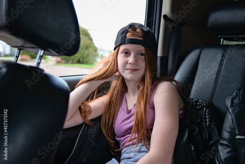 Tween girl with red hair and backwards baseball hat in car. photo