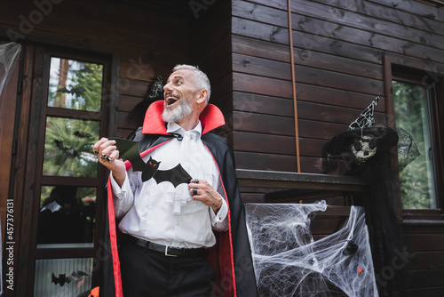 mature man in vampire halloween costume laughing on porch of decorated house