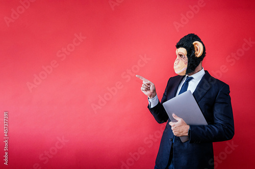 Photography Businessman in monkey mask pointing to the side with a laptop under his arm