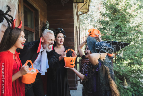 excited family in spooky halloween costumes scaring each other near house