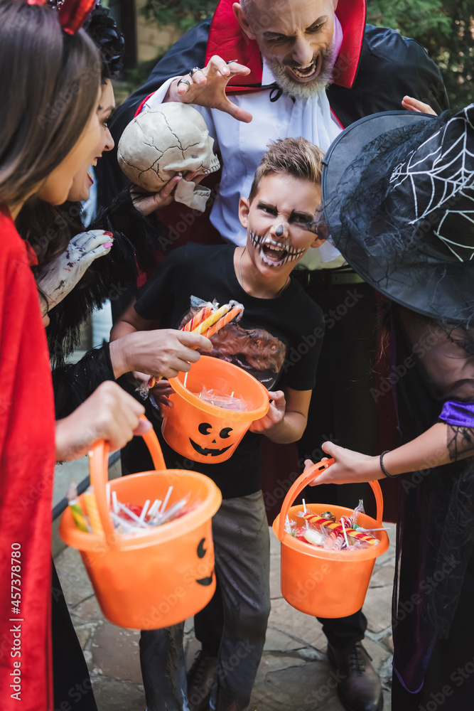 family in halloween costumes grimacing while holding buckets with sweets