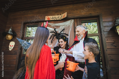 excited family in halloween costumes holding buckets with candies on house porch