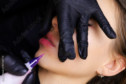 the master of permanent makeup holds his lips with his fingers and performs permanent makeup with a tattoo machine