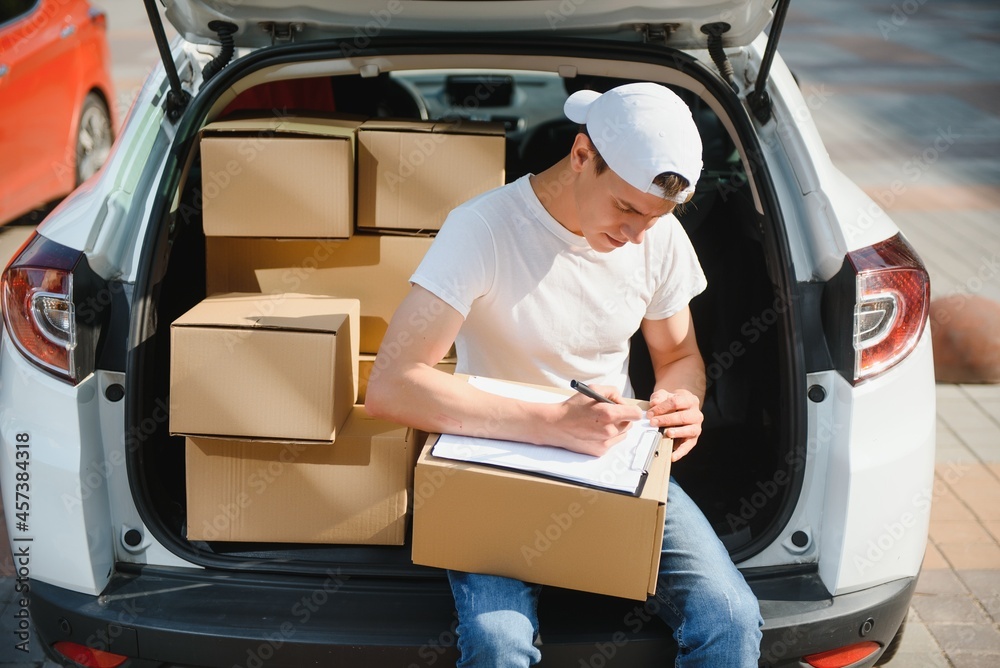 Young Delivery Man Checking List On Clipboard In car Young Delivery Man Checking List On Clipboard In car